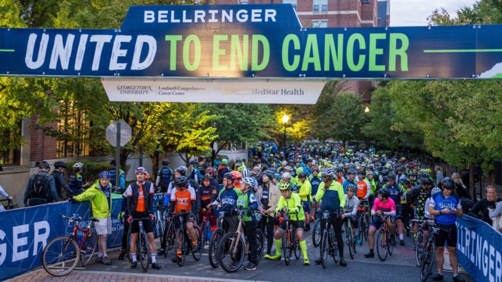 Riders mass at the starting line for BellRinger beneath an archway that reads United to End Cancer